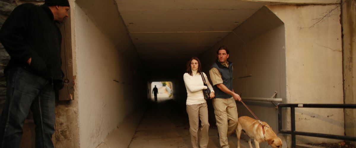 Man and Woman walking their dog through a tunnel with a guy looking at them from the shadows