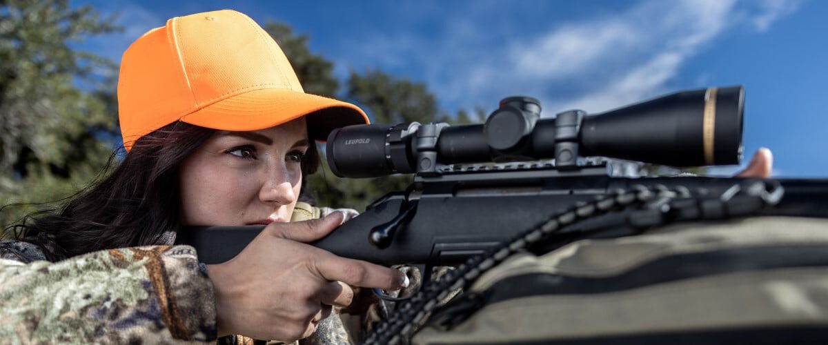 female hunter looking through the scope of a rifle