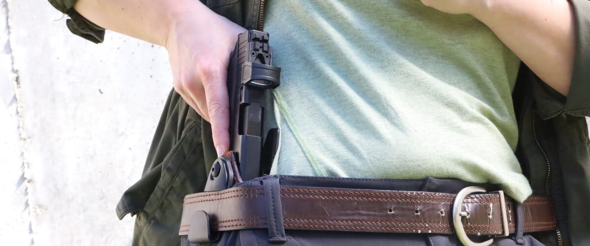 person removing a handgun from a gun holster hiding behind belt loop