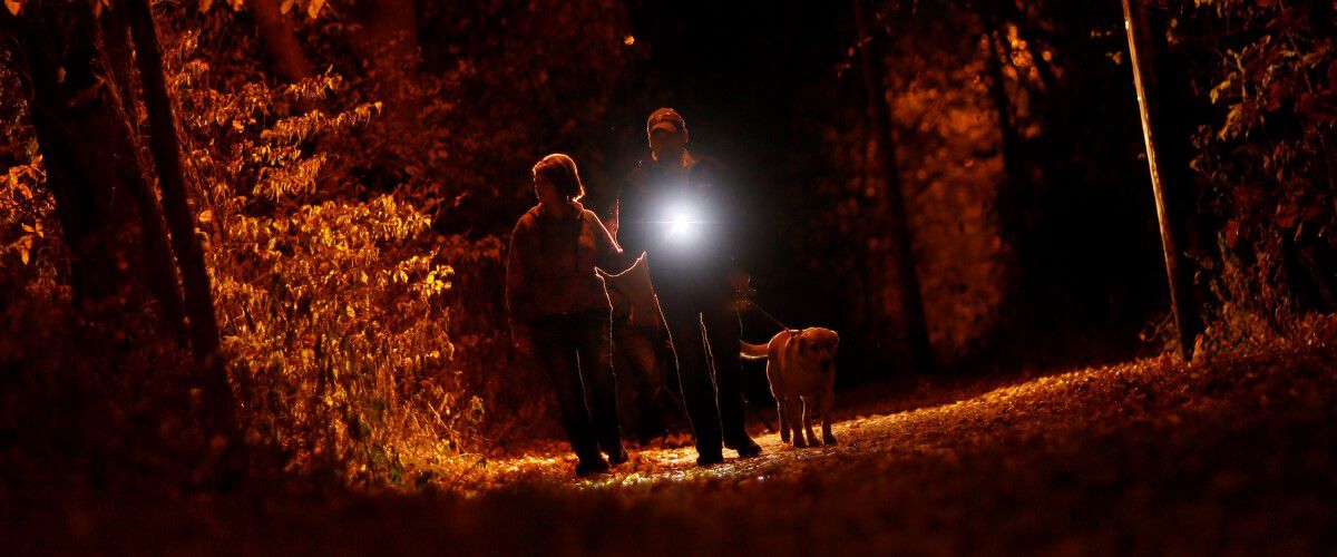 Man and Woman walking a dog in the dark while holding a flashlight