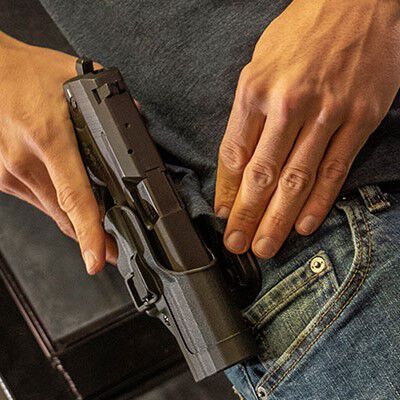 person putting pistol into a holster attached to their jeans