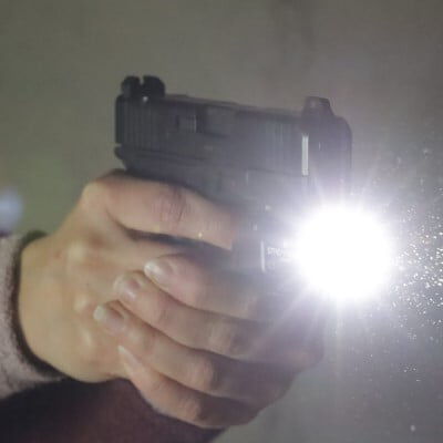 women aiming handgun with flashlight attachment