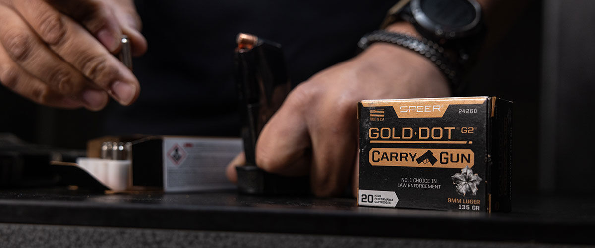 Gold Dot Carry Gun box on a table by a shooter loading a magazine