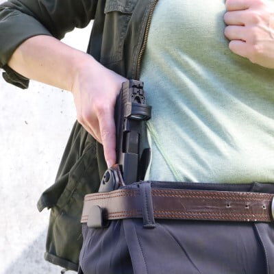 person removing a handgun from a gun holster hiding behind belt loop