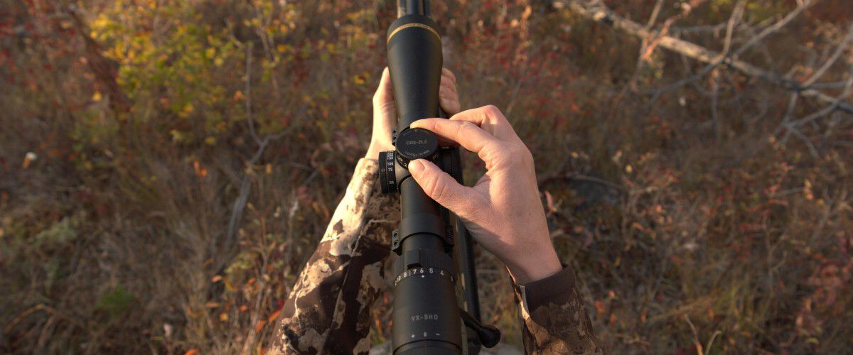 a hunter adjusting a rifle scope