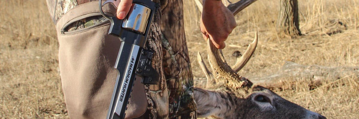 hunter holding dead deer antlers and hunting handgun