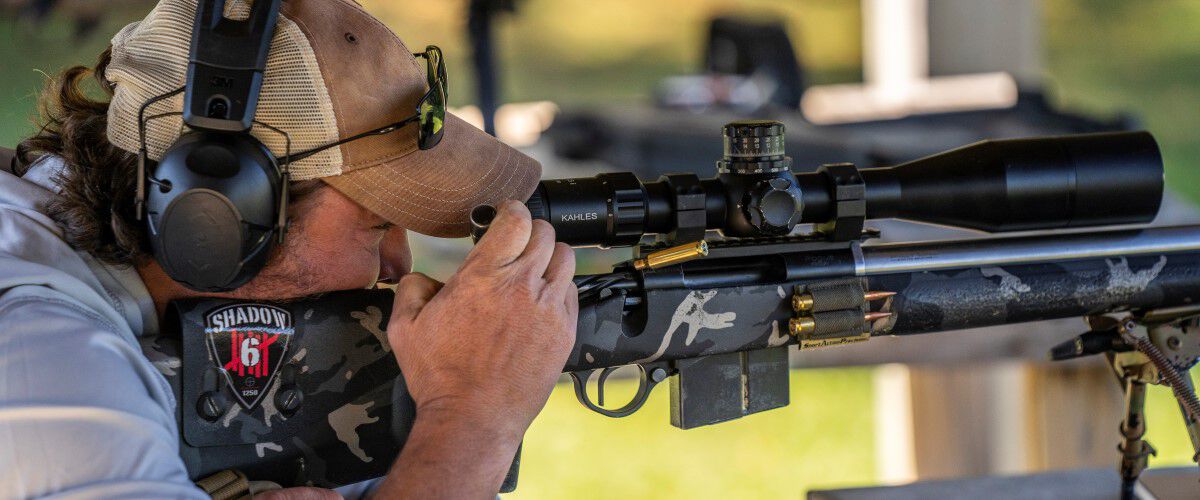 Jim Gilliland looking down the scope of a rifle resting on a bipod