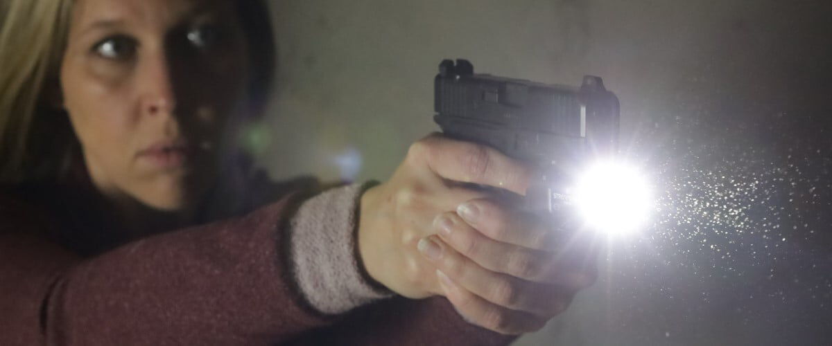 women aiming handgun with flashlight attachment