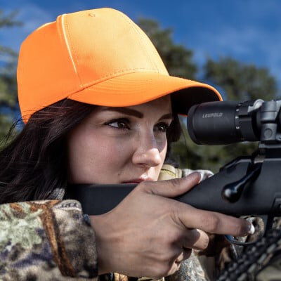 female hunter looking through the scope of a rifle